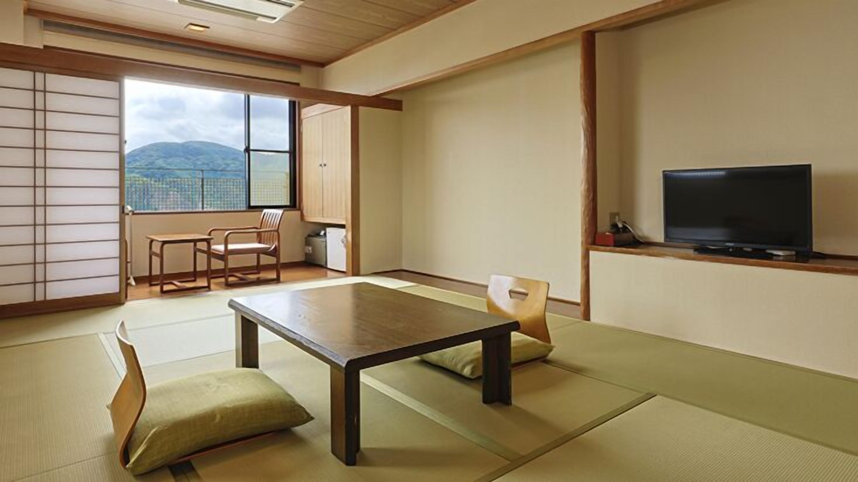 Et traditionelt japansk rum med tatami-gulv, et lavt bord, et fjernsyn og udsigt til bjerge.