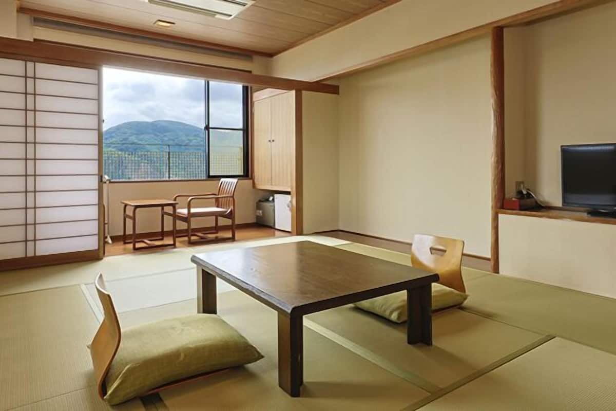 A traditional Japanese room with tatami flooring, a low table, a television, and a view of mountains.
