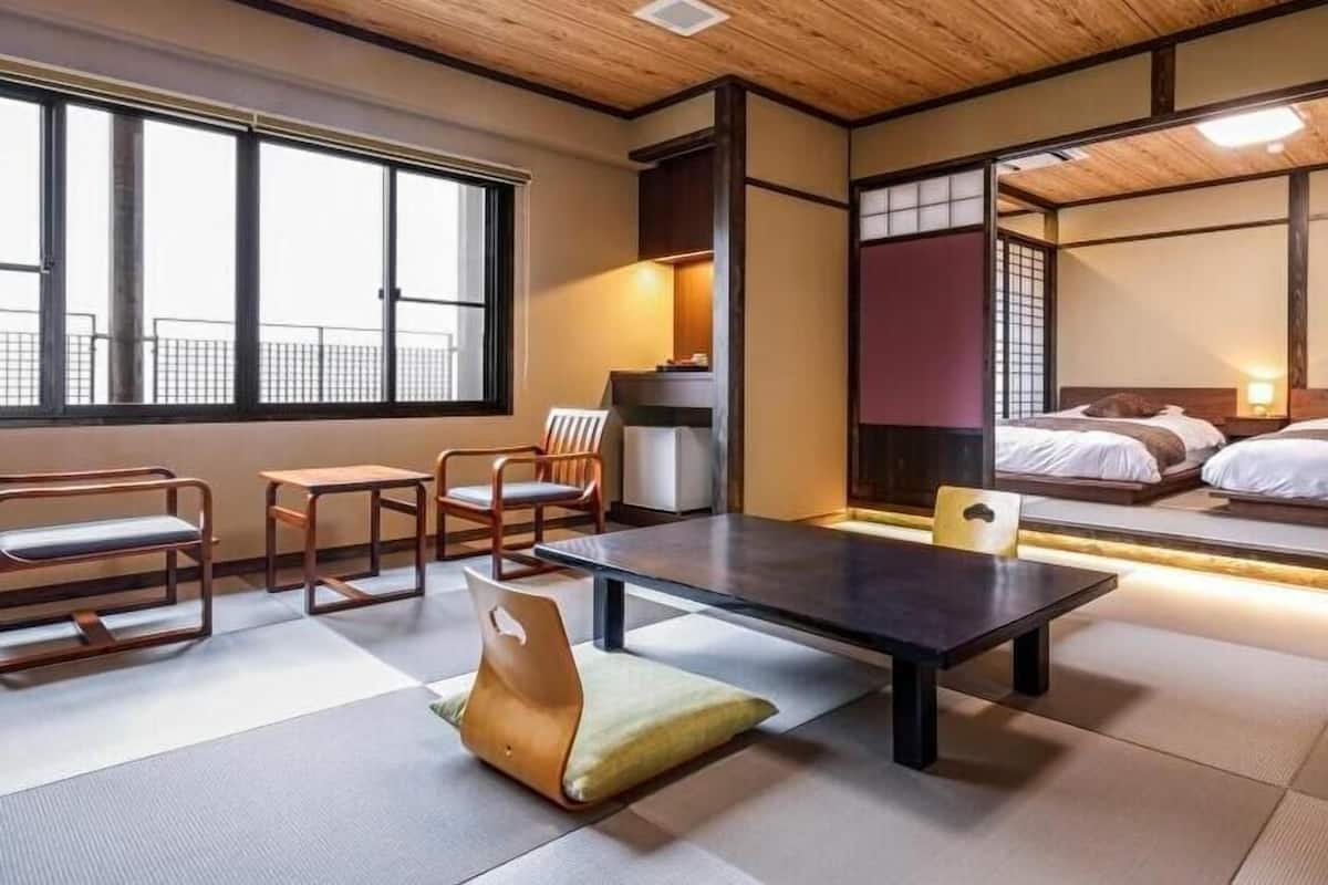 A traditional Japanese-style room with tatami flooring, a low table, chairs, and a bed with a view of the city.