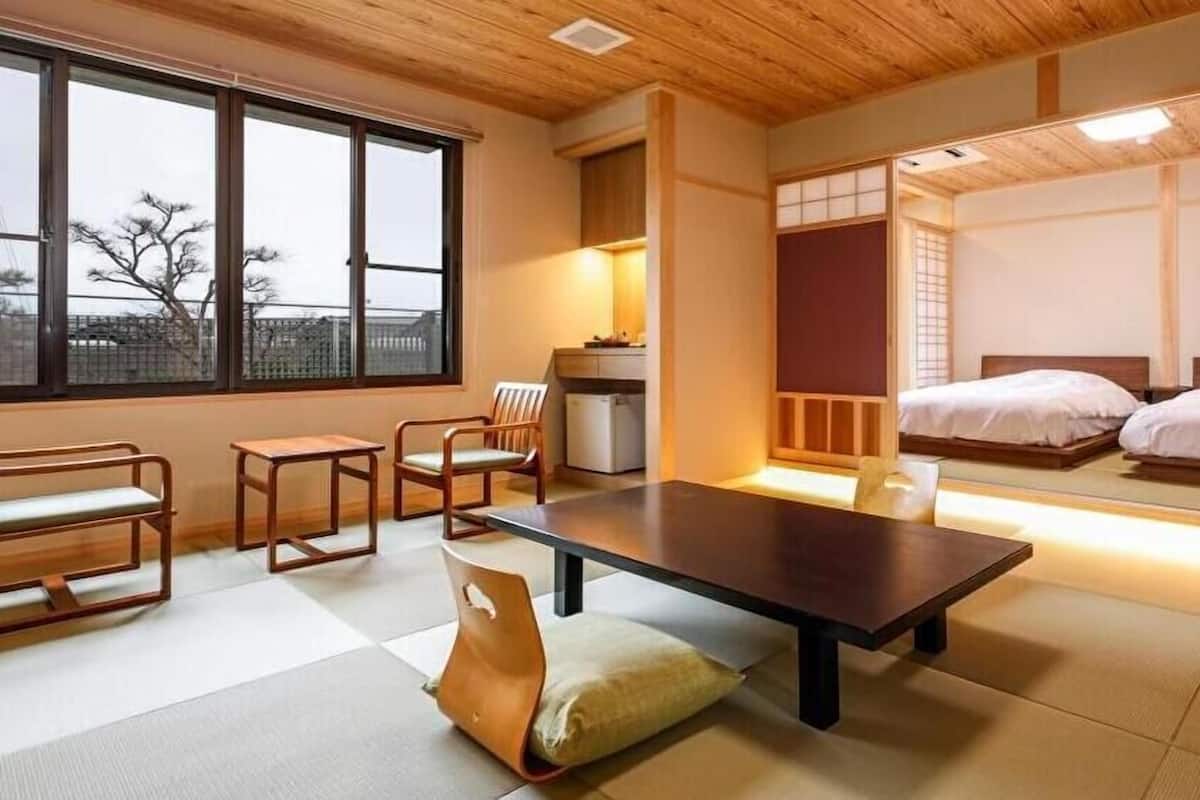 A traditional Japanese-style room with tatami flooring, a low table, a chair, and a bed with a futon.
