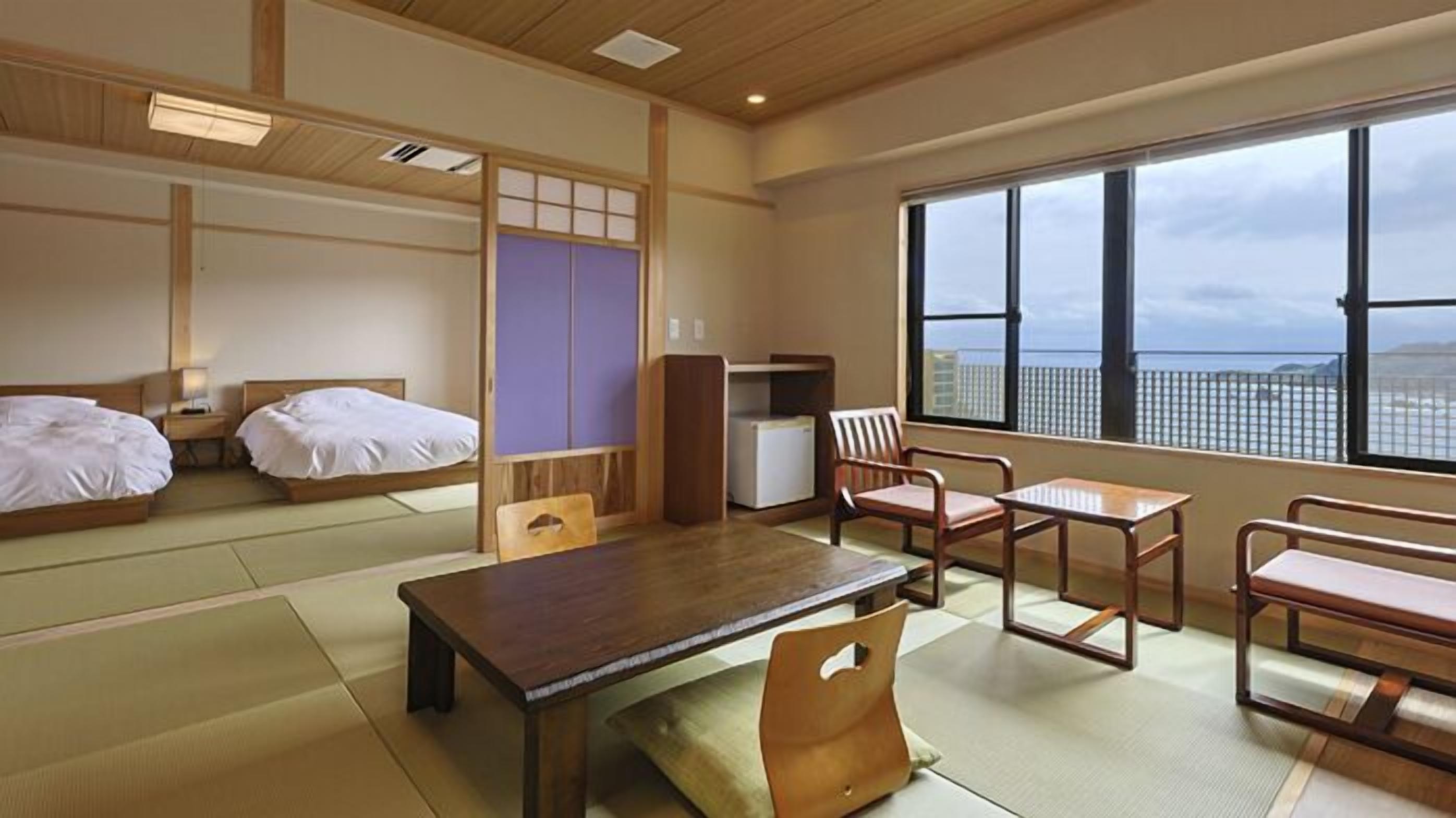 A traditional Japanese-style room with tatami flooring, a low table, two wooden chairs, a small cabinet, and a window with a view.