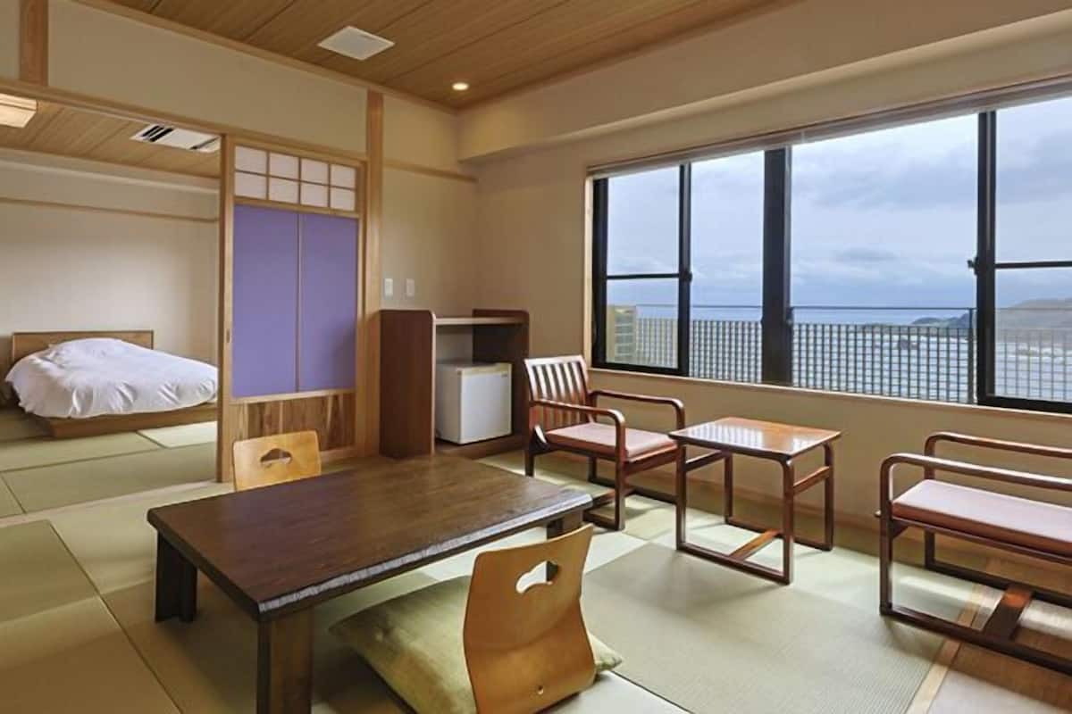 A traditional Japanese-style room with tatami flooring, a low table, two wooden chairs, a small cabinet, and a window with a view.