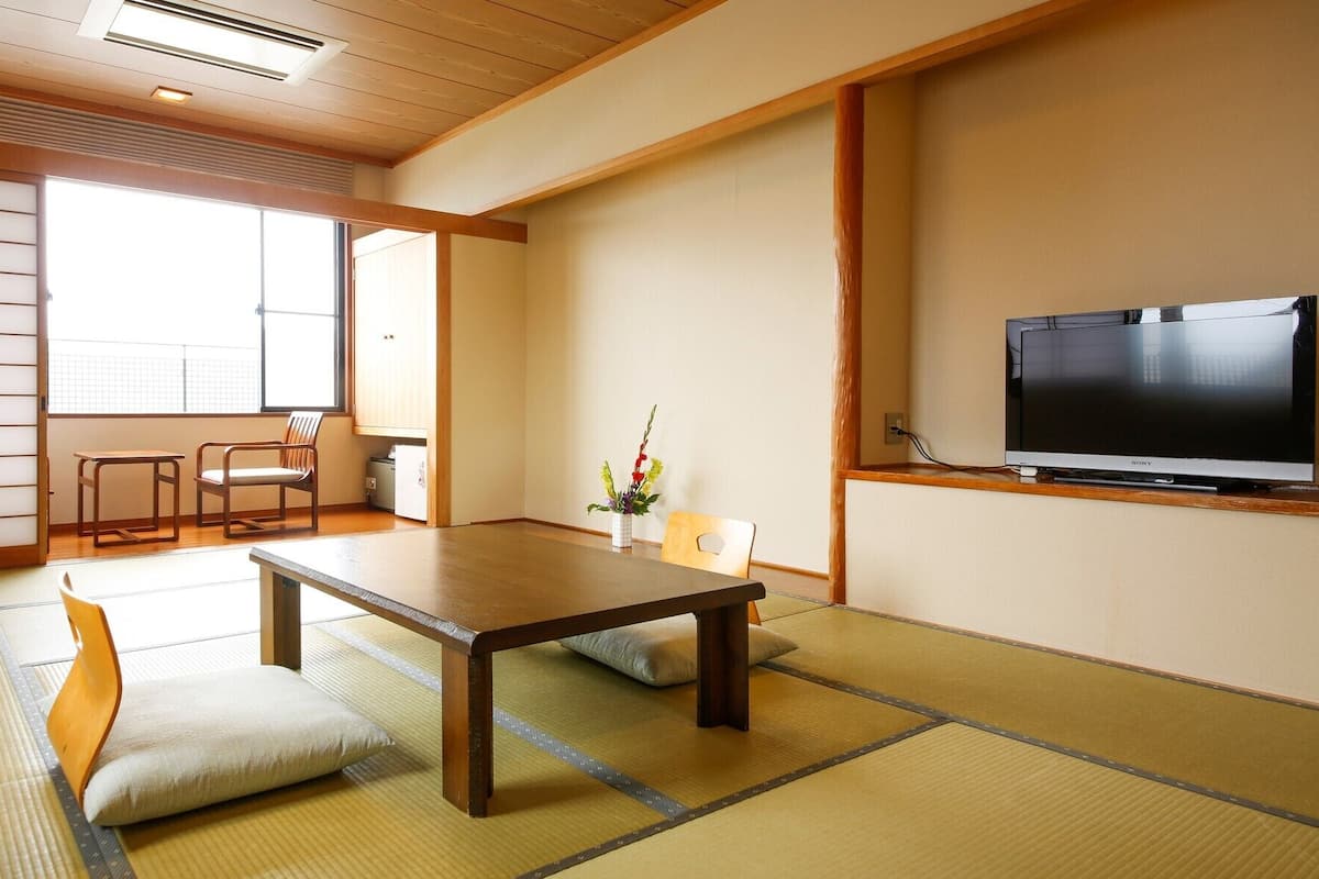 A traditional Japanese room with tatami flooring, a low table, a television, and sliding doors.