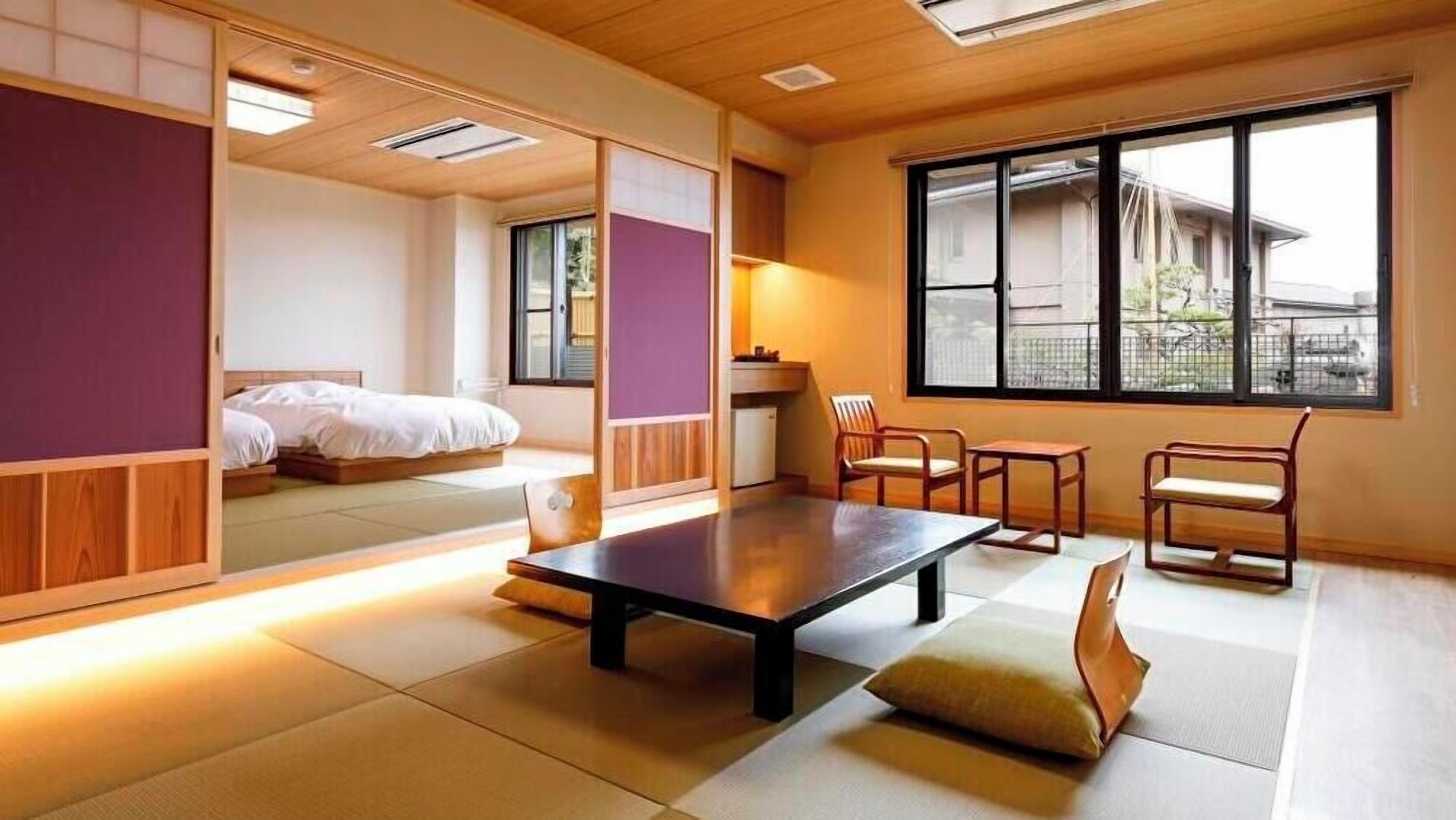 A traditional Japanese-style room with tatami flooring, a low table, and a bed with a futon.