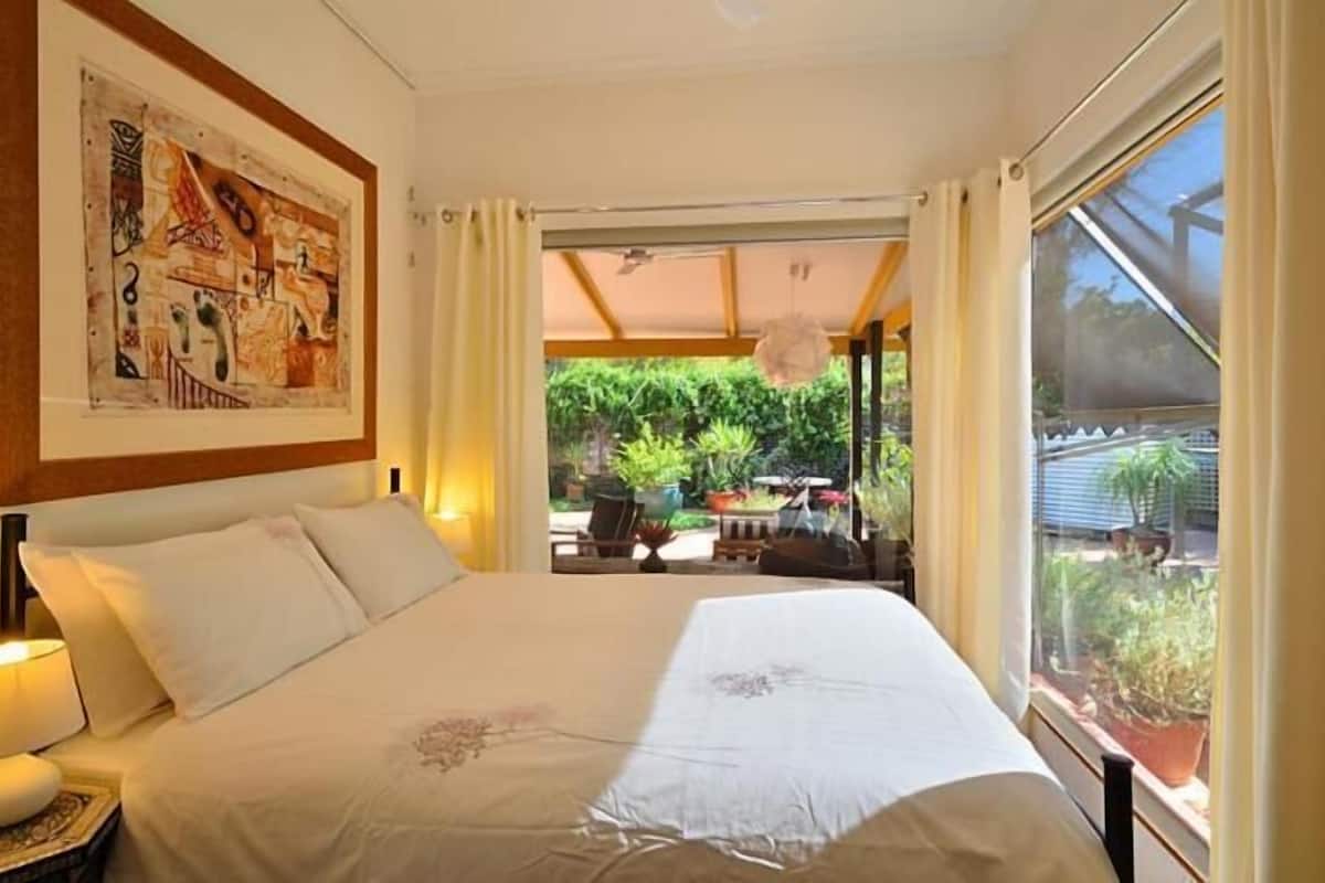 A bedroom with a large bed, a ceiling fan, and a view of a garden through a sliding door.