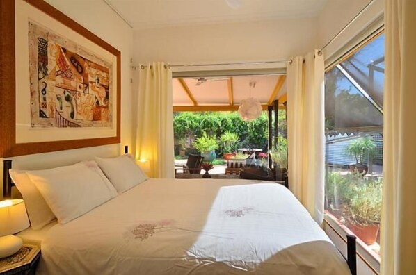 A bedroom with a large bed, a ceiling fan, and a view of a garden through a sliding door.