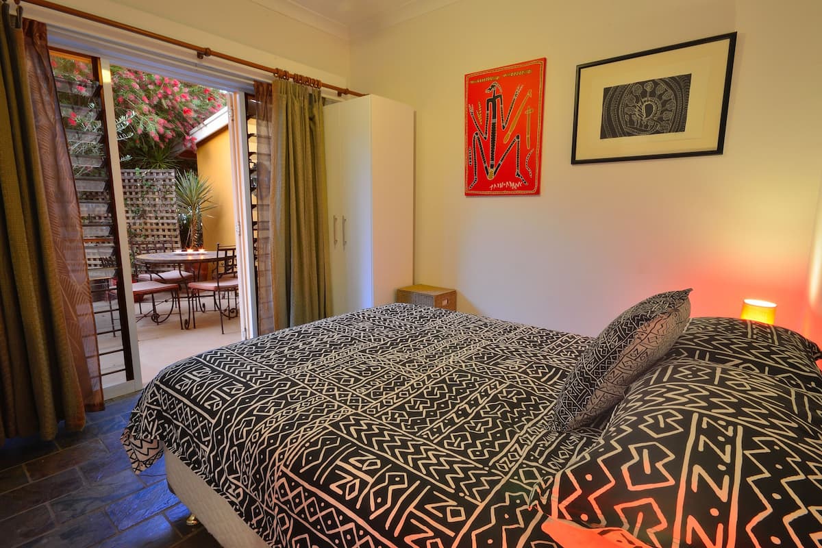 A bedroom with a patterned bedspread, a desk with a chair, and a dining area with a table and chairs.