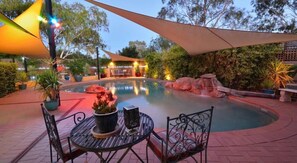 A pool area with a table and chairs, surrounded by potted plants and a large umbrella.