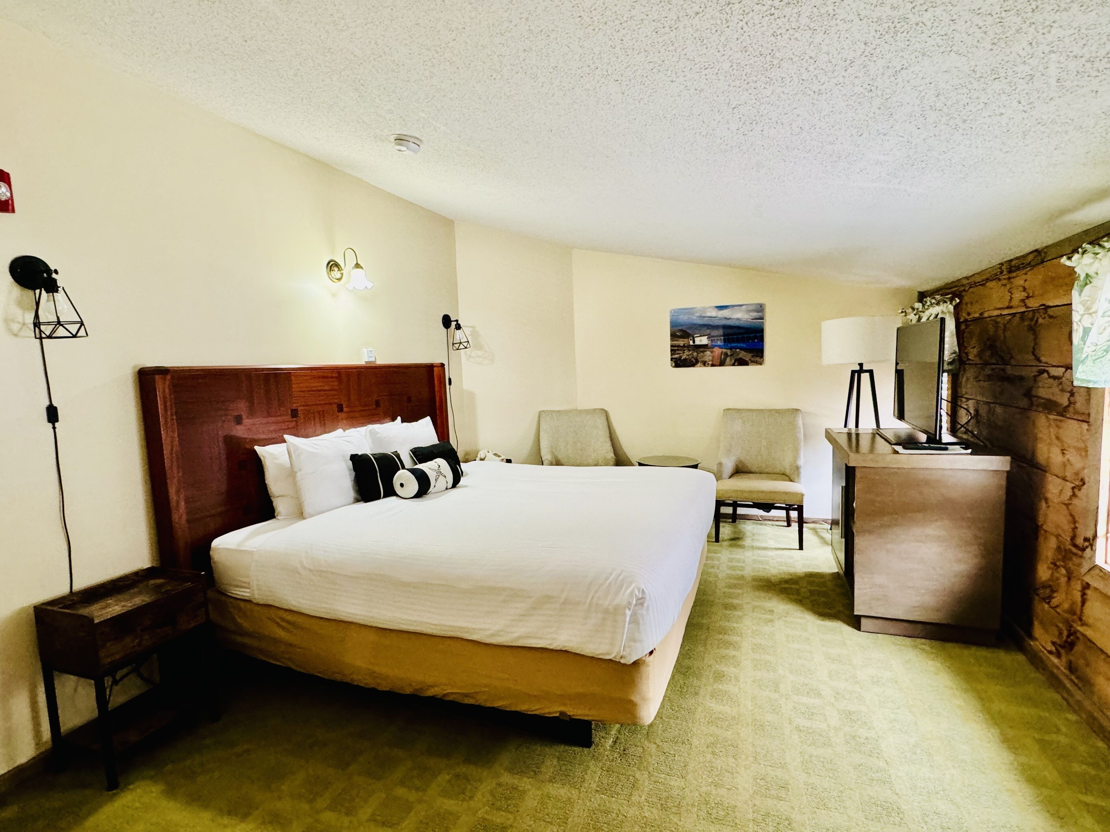 A hotel room with a large bed, a desk, a chair, and a small table.