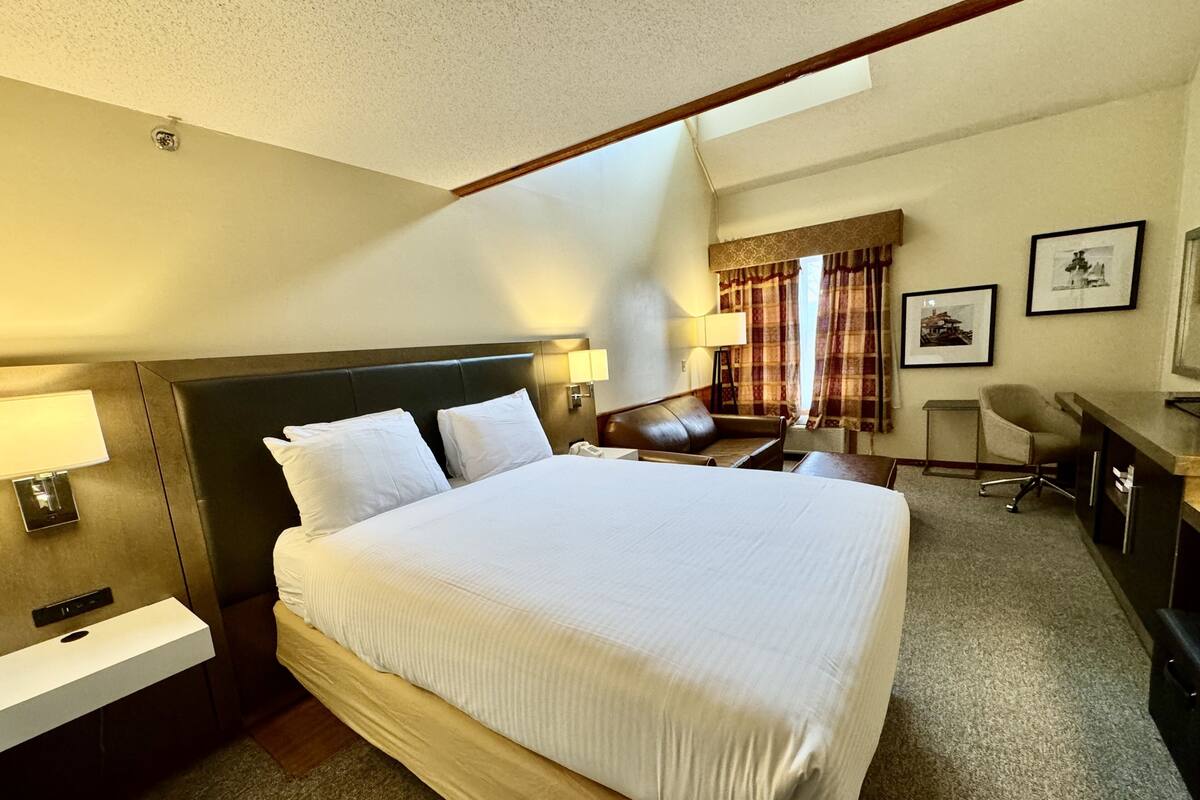 A hotel room with a large bed, bedside tables, a desk, a chair, and a window with curtains.