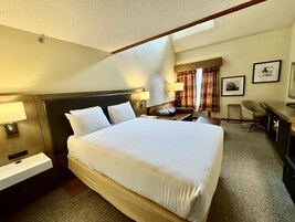 Habitación de hotel con una cama grande, mesitas de noche, un escritorio, una silla y una ventana con cortinas.