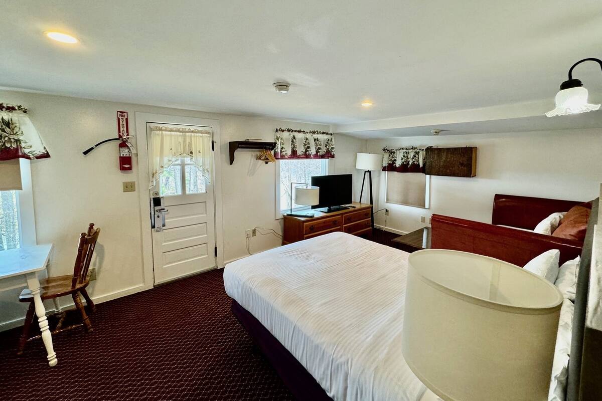 A hotel room with a large bed, a desk with a chair, a television, and a lamp.