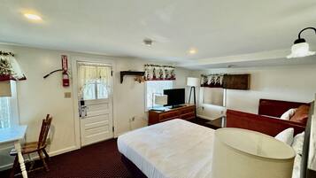 Quarto de hotel com uma cama grande, uma escrivaninha com cadeira, televisão e luminária.