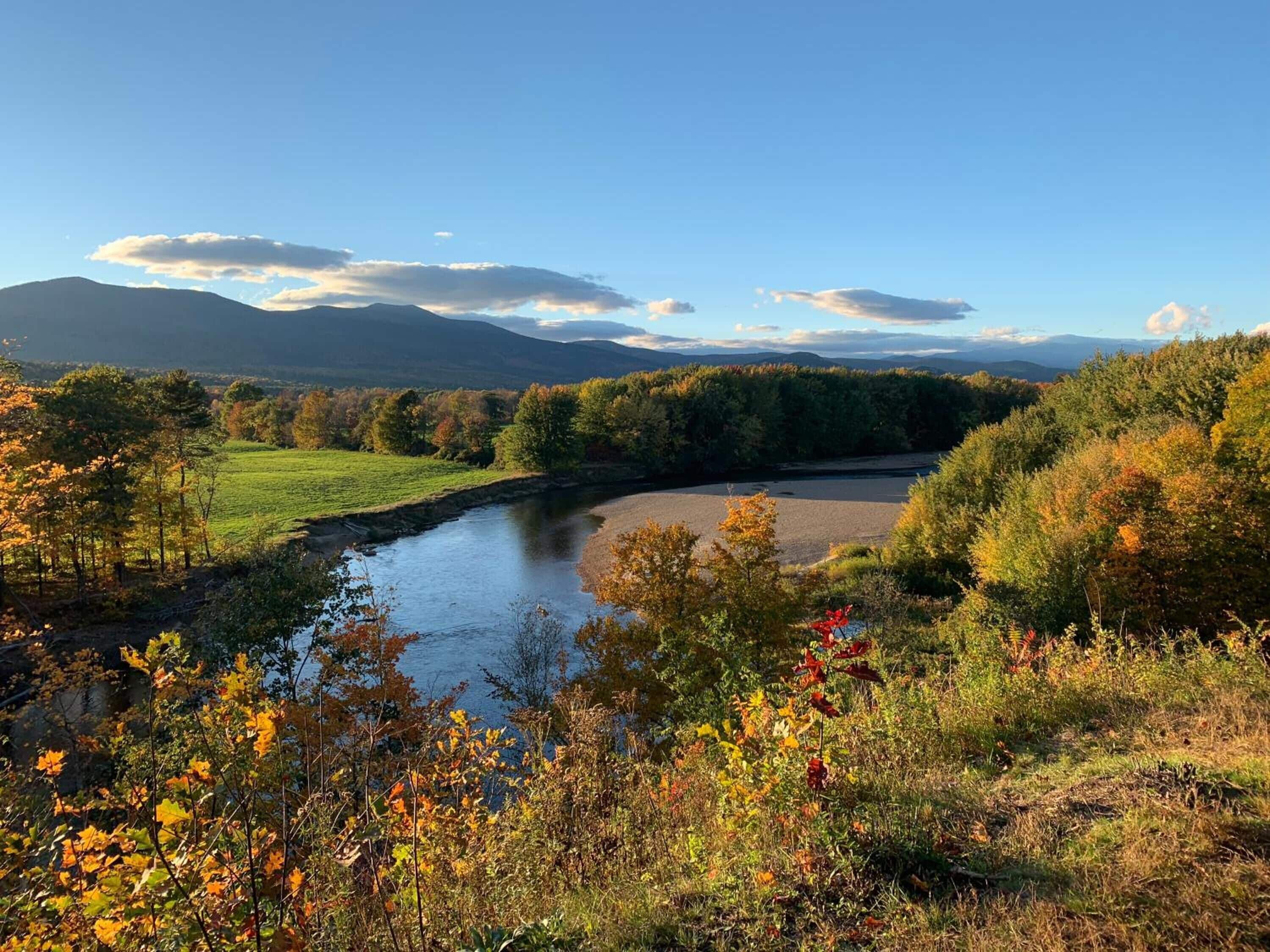 A river flowing through a valley with autumn foliage and distant mountains.