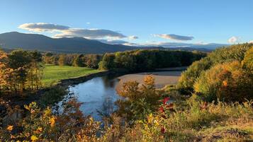 A river flowing through a valley with autumn foliage and distant mountains.