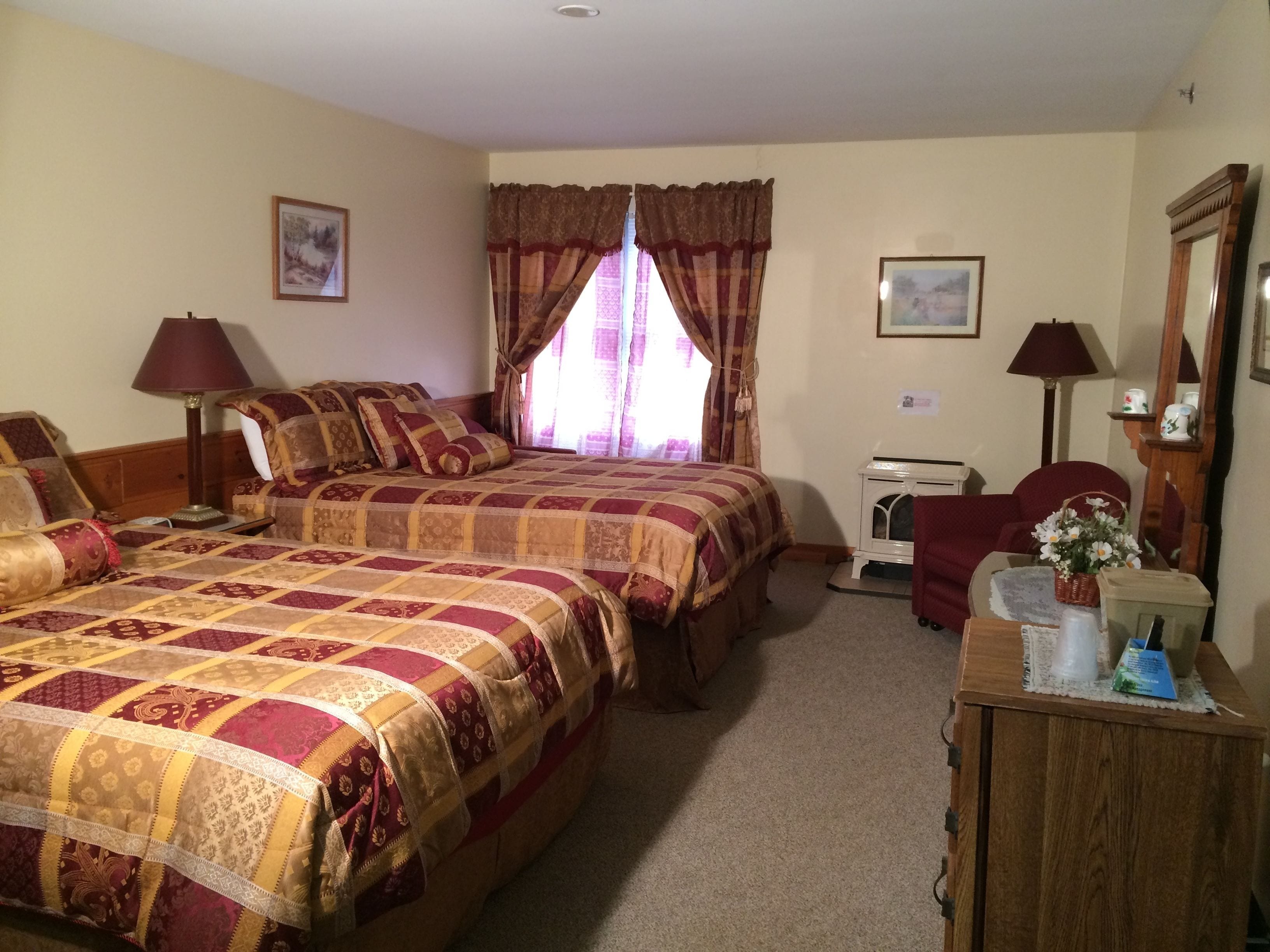A hotel room with two beds, a desk, a chair, a lamp, a mirror, and a window with curtains.
