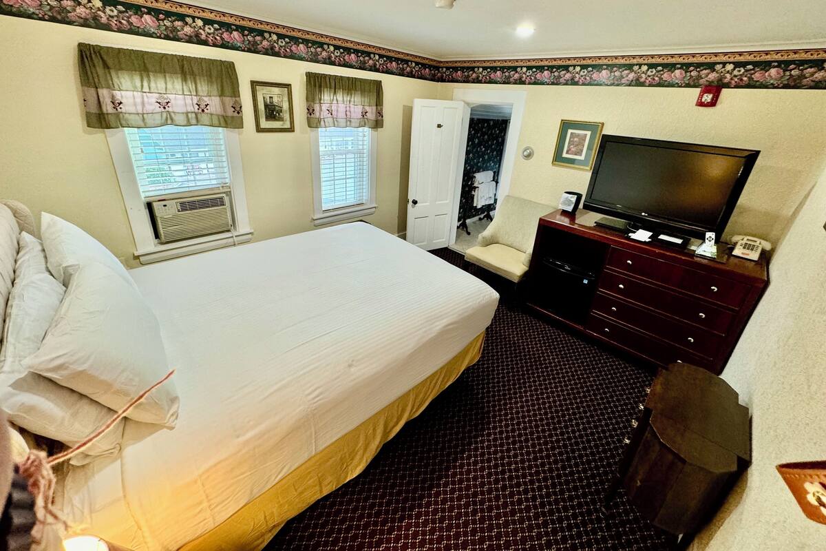 A hotel room with a large bed, a television, a dresser, and a chair.