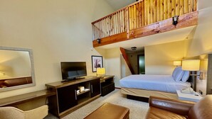 Ein Hotelzimmer mit Bett, Fernseher, Schreibtisch mit Computer, Stuhl und kleinem Tisch.