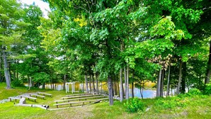 Ein Park mit Picknicktischen, einer Holzbank und einem Teich, der von Bäumen umgeben ist.