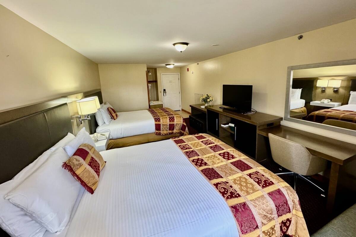 A hotel room with two beds, a desk with a TV, a mirror, and a small bathroom.
