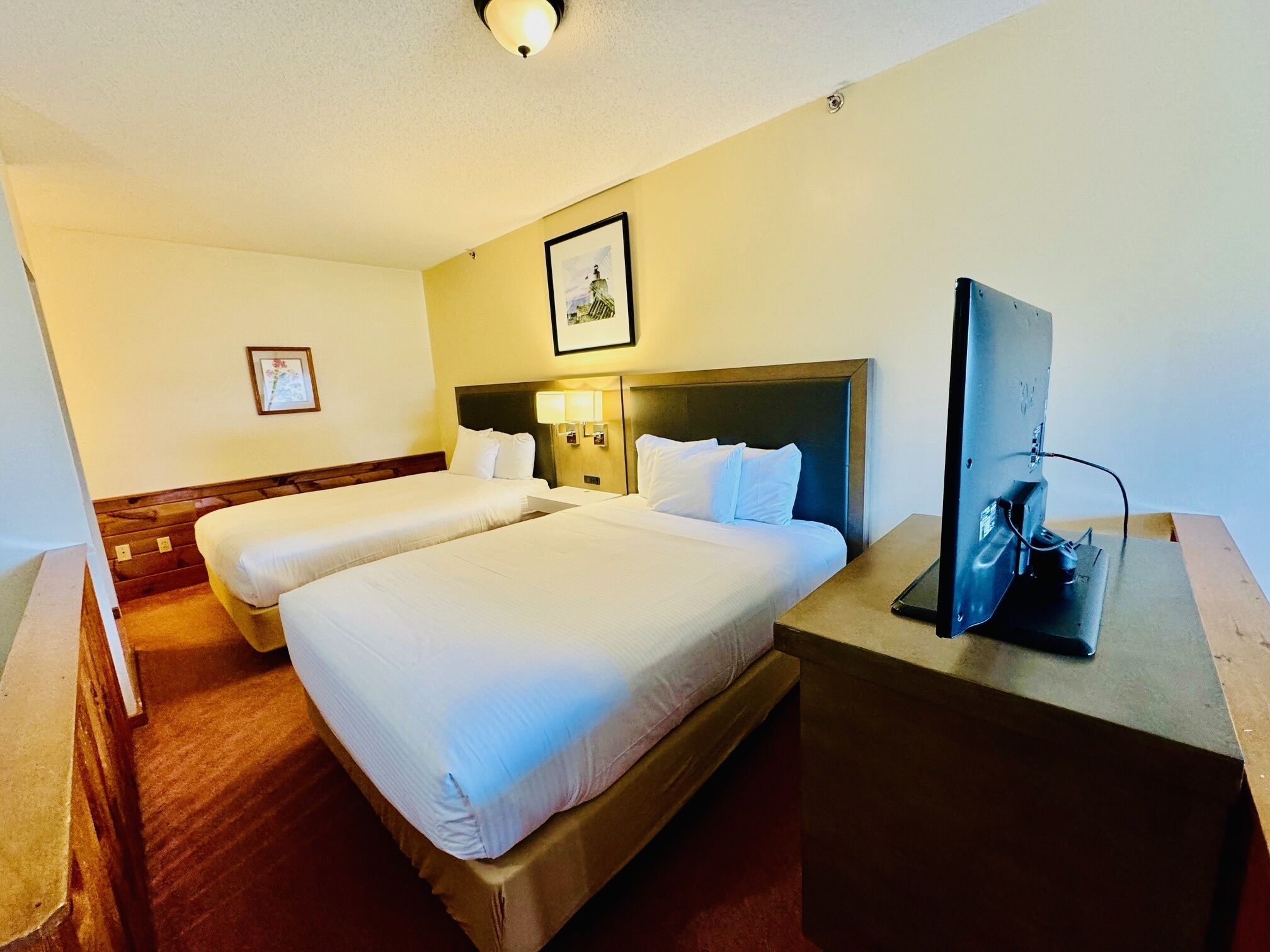 A hotel room with two beds, a TV, and a framed picture on the wall.