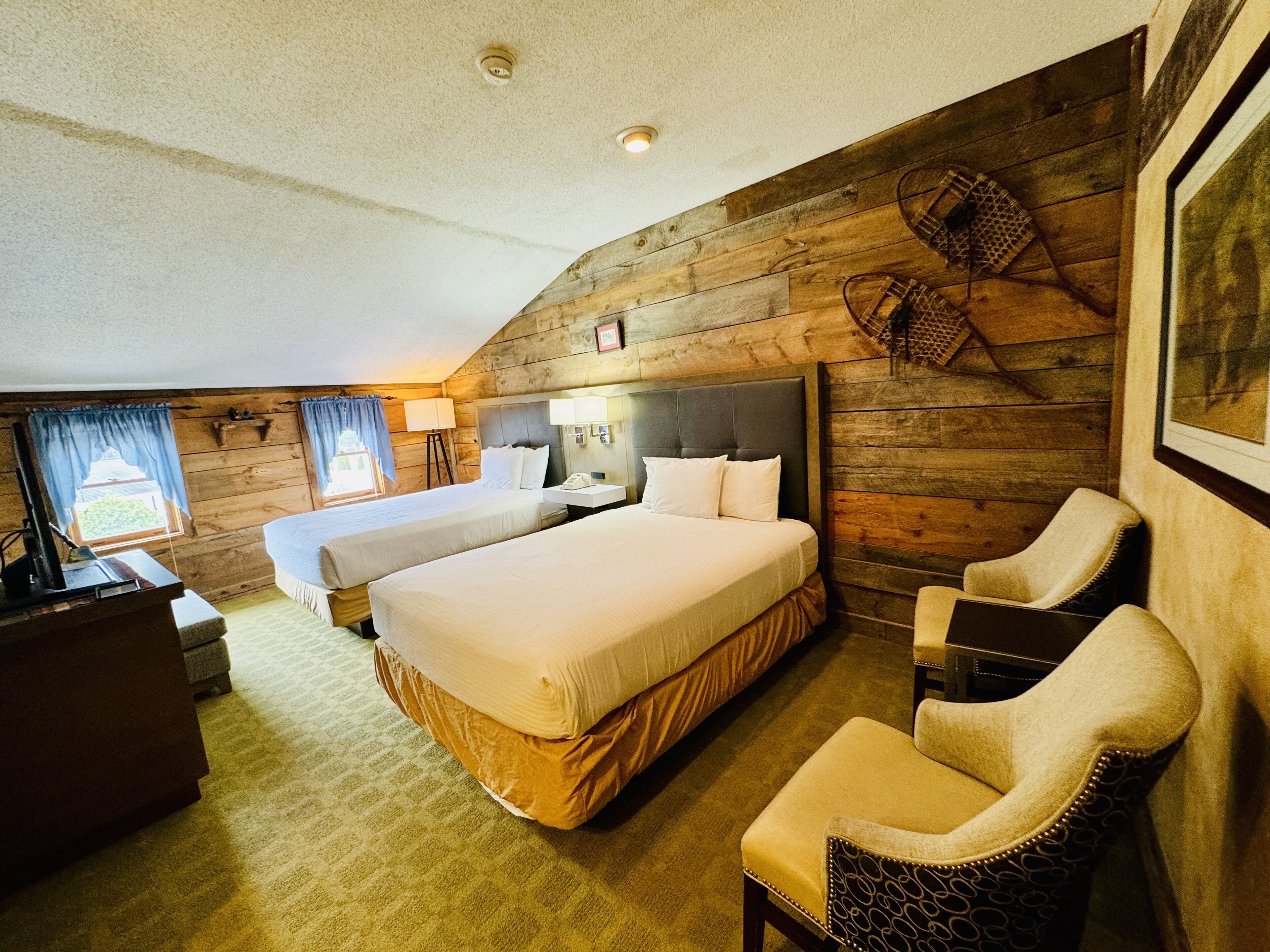 A hotel room with two beds, a desk, a chair, and a large window.