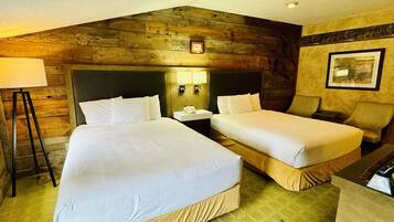 A hotel room with two beds, a nightstand, a lamp, and a framed picture on the wall.