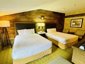 A hotel room with two beds, a nightstand, a lamp, and a framed picture on the wall.