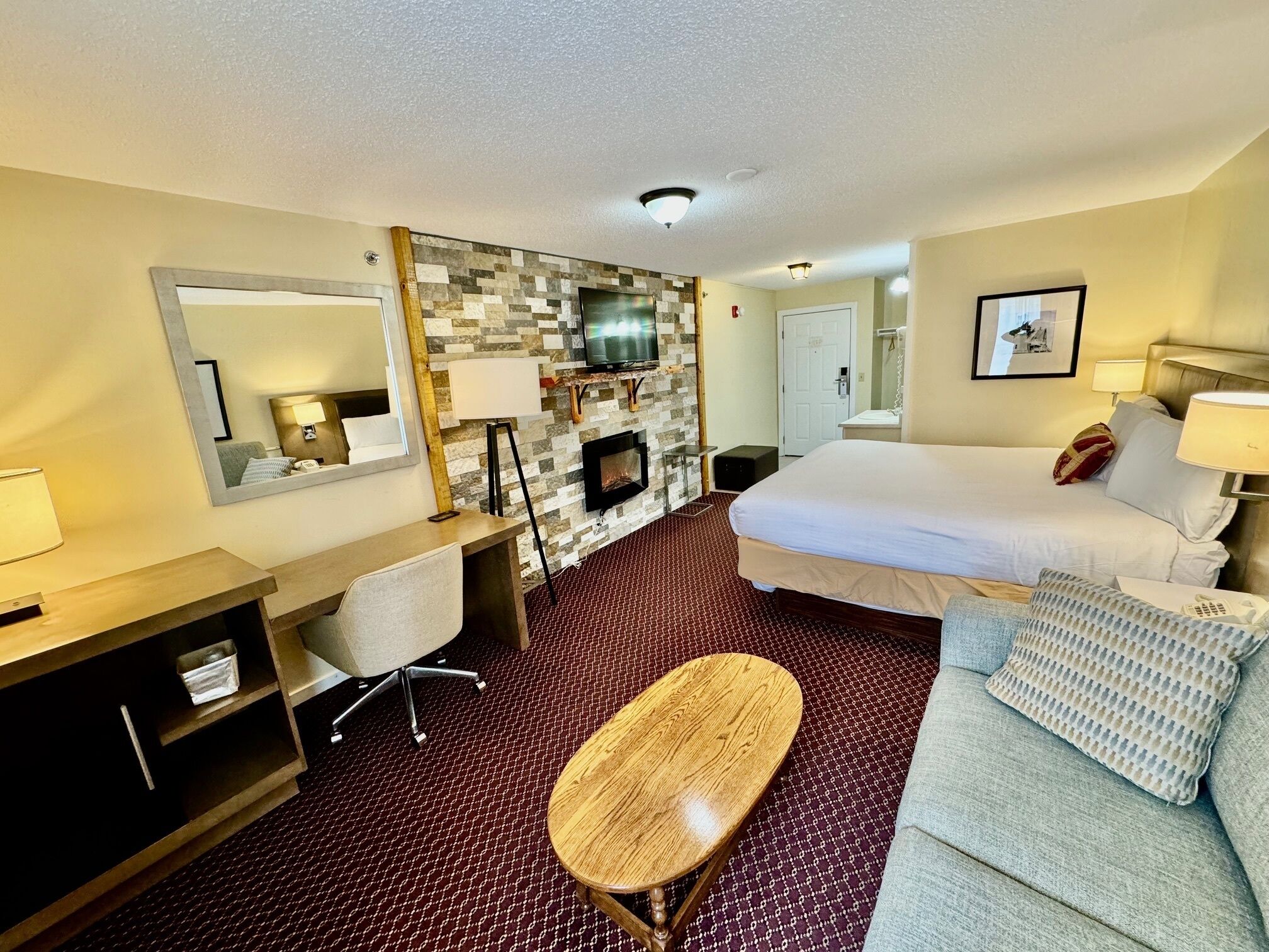 Una habitación de hotel con cama, escritorio, silla, televisión y chimenea.
