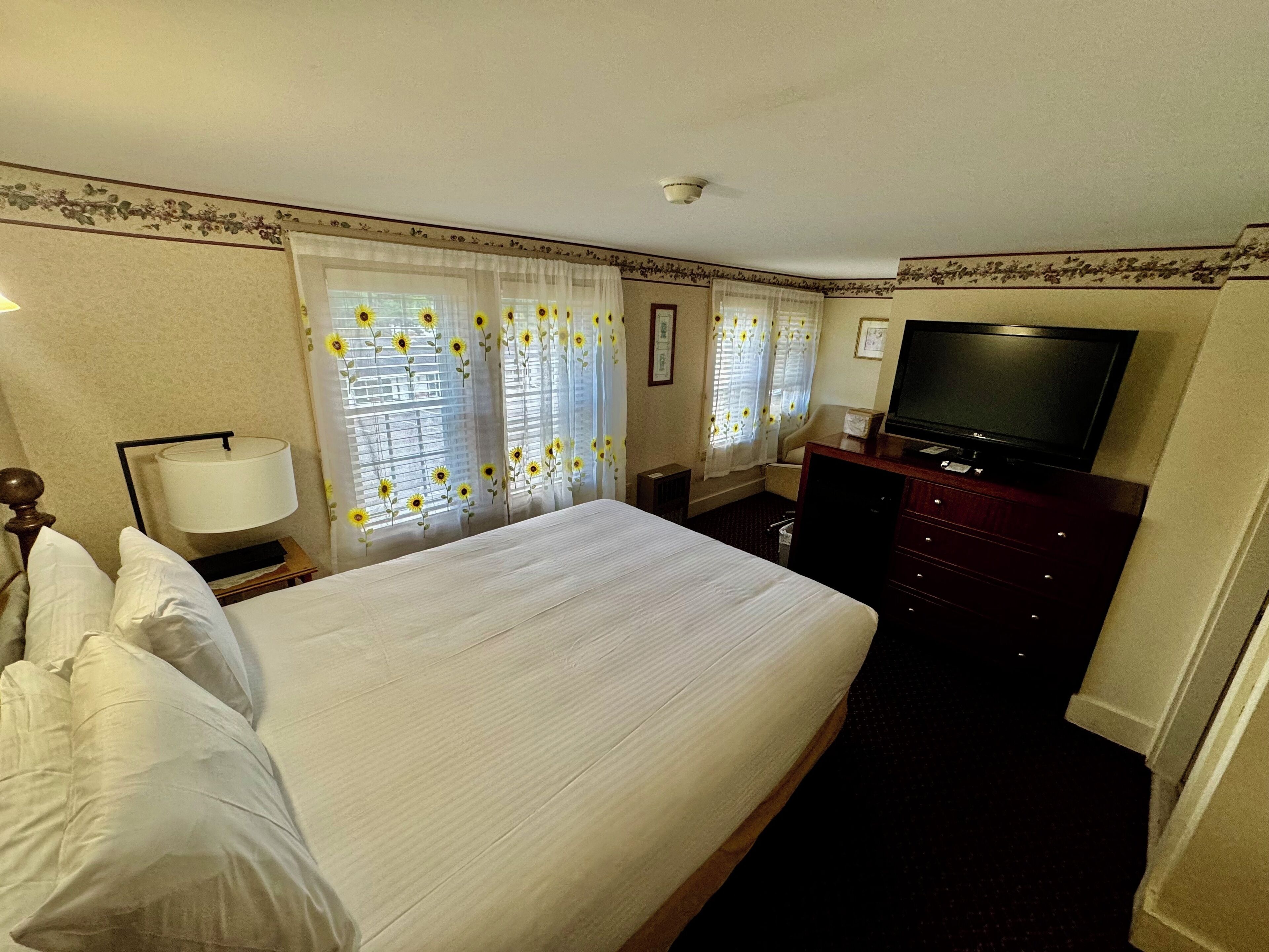 Quarto de hotel com uma cama grande, televisão, penteadeira e abajur.