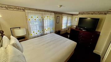 Quarto de hotel com uma cama grande, televisão, penteadeira e abajur.