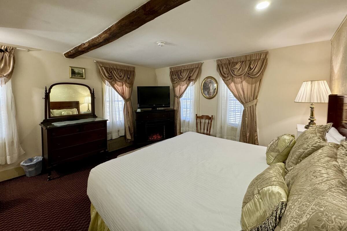 A bedroom with a large bed, a dresser, a television, and a lamp.