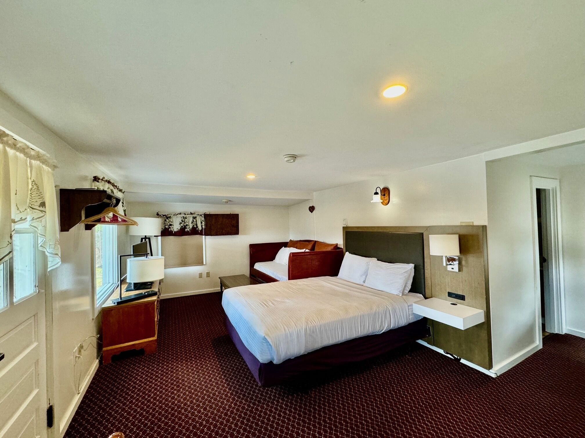 A hotel room with a bed, bedside table, lamp, and a wall-mounted shelf.