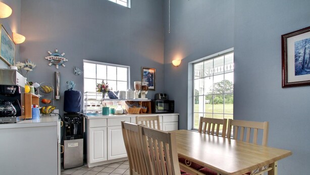 A compact kitchen with white cabinets, a wooden dining table, and chairs. There is a window providing natural light and a view of the outdoors. - Key West Inn - Lafayette (LaFayette)