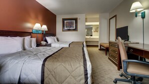 A hotel room with two beds, a desk, a chair, a dresser, a lamp, a painting, and a mirror. - Key West Inn - Lafayette (LaFayette)