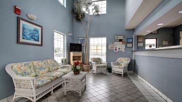 A room with a blue wall, a white wicker sofa, a white coffee table, and a television.