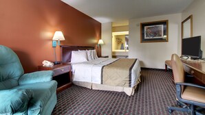 A hotel room with a bed, a desk, a chair, a lamp, a television, and a framed picture on the wall. - Key West Inn - Lafayette (LaFayette)