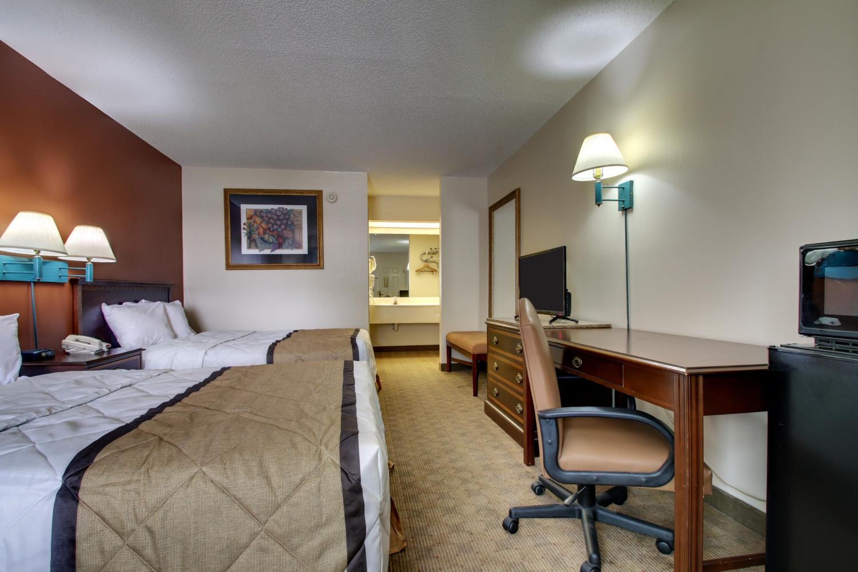 Een hotelkamer met twee bedden, een bureau, een stoel, een televisie en een badkamer in de achtergrond.