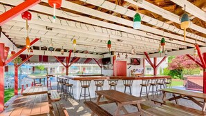 An outdoor dining area with wooden tables and chairs, a bar counter, and hanging decorative lights. - The Rhumb Line Resort (Kennebunkport)