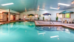 A swimming pool with a tiled edge, indoor seating area with tables and chairs, and ceiling lights. - The Rhumb Line Resort (Kennebunkport)