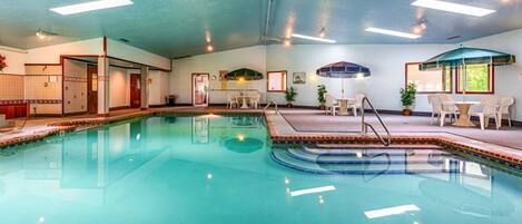 A swimming pool with a tiled edge, indoor seating area with tables and chairs, and ceiling lights.