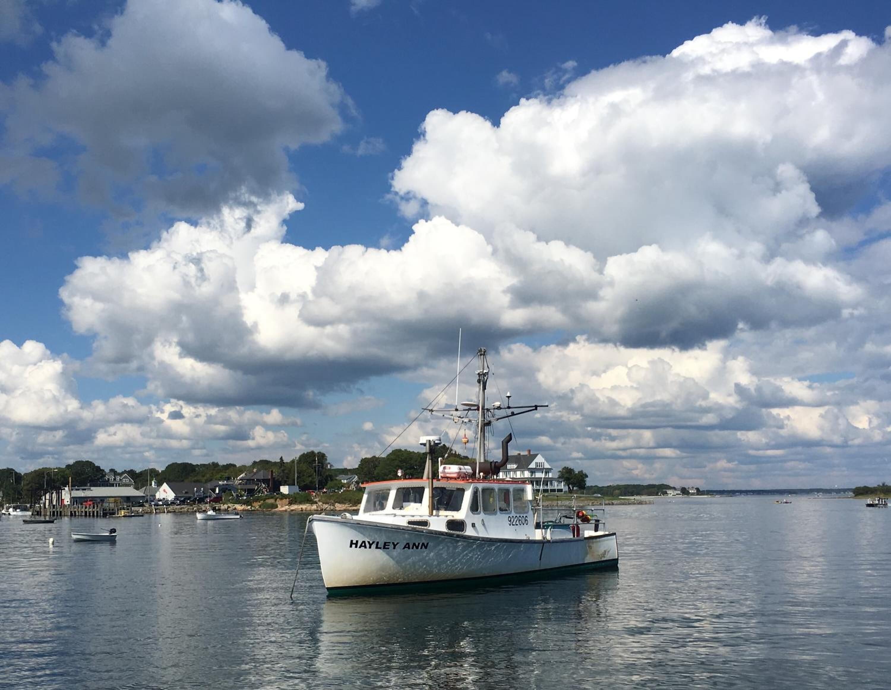 A boat named 'Hayley Ann' docked at a harbor with a backdrop of clouds and a distant shoreline.