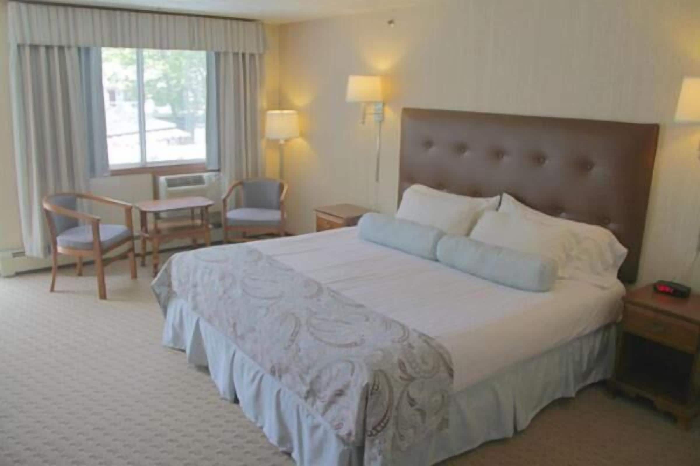 Una habitación de hotel con una cama grande, dos mesitas de noche, un escritorio con sillas y una ventana con cortinas.
