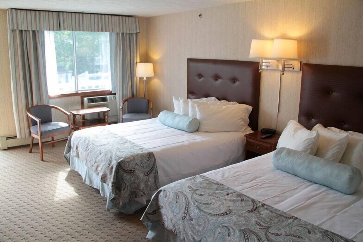 A hotel room with two beds, a desk, a chair, and a window with curtains.