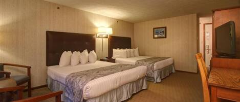 A hotel room with two beds, a desk, a chair, a television, and a nightstand with a lamp.