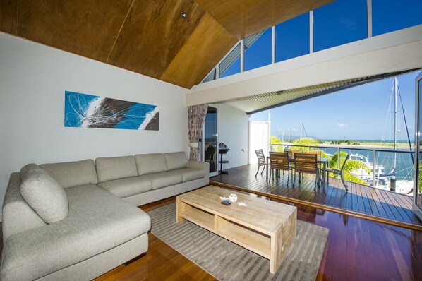 A modern living room with a large sofa, a coffee table, and a view of the sea through large windows.