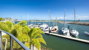 A marina with several sailboats docked at the pier, surrounded by lush greenery and a clear blue sky. - Waters Edge Townhouse 4 (Nelly Bay)