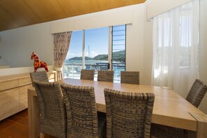 A dining area with a wooden table and wicker chairs, large windows with a view of the sea and hills, and a decorative horse figure on the left.
