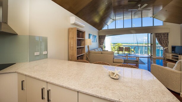 A modern kitchen with a large island, a dining area with a view, and a living space with a TV and seating. - Waters Edge Townhouse 4 (Nelly Bay)