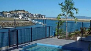 A swimming pool with a view of a coastal area, including a bridge and buildings. - Waters Edge Townhouse 4 (Nelly Bay)